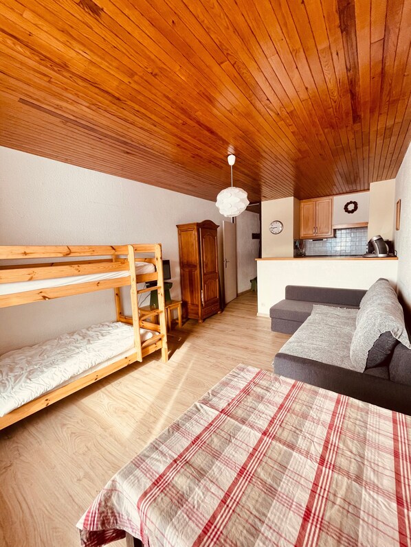 Ein gemütliches Zimmer mit Etagenbett, einer Schlafcouch, einer Küchenzeile und einer Holzbalkendecke.