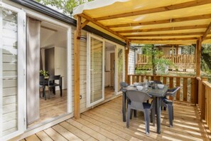 Eine überdachte Terrasse mit Tisch und Stühlen, eine Glasschiebetür zu einem Innenraum und ein Holzdeck.