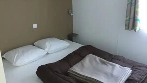Una cama individual con almohadas blancas y una manta marrón, una mesita de noche y una lámpara fijada a la pared.