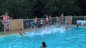 Una piscina con gente nadando y sentada en el borde, rodeada por una valla.