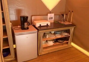 Eine kleine Küchenzeile mit Kühlschrank, Kaffeemaschine und einer Anrichte mit Geschirr.