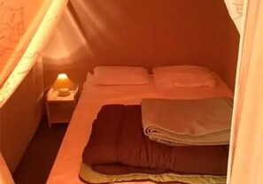 Ein kleines, gemütliches Zimmer mit einem Einzelbett, einem Nachttisch mit Lampe und einer über dem Bett gespannten Zeltkonstruktion.