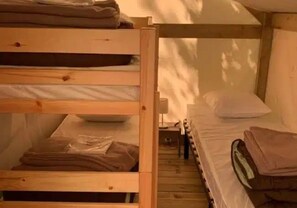 Ein Schlafraum mit Etagenbetten, Holzboden und einem Einzelbett mit Kissen.