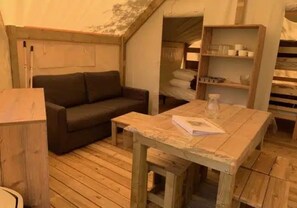 Ein Zimmer mit Holzboden, einer Couch, einem kleinen Tisch mit einem Buch und einem Regal mit Tassen.