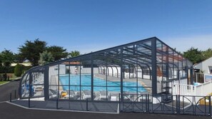 Ein überdachter Swimmingpool mit Glasveranda, umgeben von Liegestühlen und einem weißen Zaun.