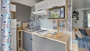 Cocina compacta con microondas, estufa y pileta, un pequeño comedor con mesa y sillas, y una sala de estar con sofá y planta.