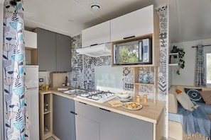 Eine kompakte Küche mit Mikrowelle, Herd und Spüle, ein kleiner Essbereich mit Tisch und Stühlen sowie ein Wohnbereich mit Sofa und Pflanze.