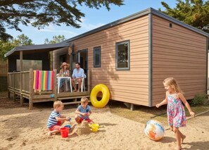 Eine Holzhütte mit einer Terrasse, einem Sandspielplatz für Kinder und einem großen Luftreifen.