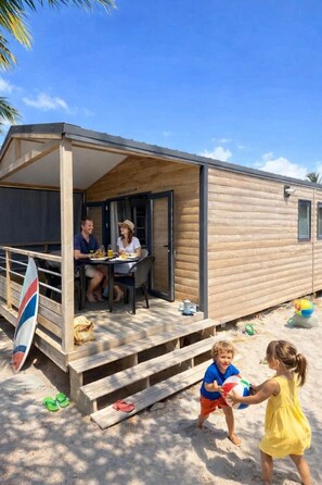 Une maison mobile en bois avec un patio couvert, une planche de surf et des enfants qui jouent.