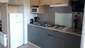 Een kleine keuken met een koelkast, magnetron, fornuis en een klein spoelbakje.
