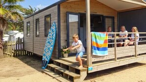 Een houten blokhut met een overdekte veranda, een surfboard daar tegenaan en een strand in de achtergrond.