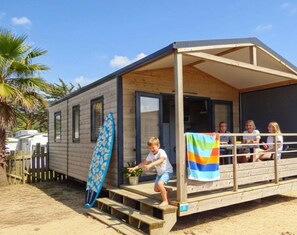 Eine Holzhütte mit überdachter Veranda, ein Surfbrett, das dagegen lehnt, und eine Strandkulisse.