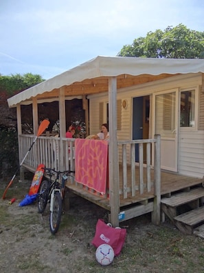 Eine Holzterrasse mit überdachter Veranda, einem Fahrrad und einer Tasche am Boden.