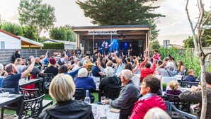 Evento al aire libre con escenario y público sentado en mesas.