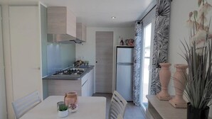 Une cuisine moderne équipée d’une cuisinière à gaz, d’un four encastré et d’un réfrigérateur. On y trouve une table à manger avec des chaises, une fenêtre avec des rideaux et des vases décoratifs posés sur le rebord de la fenêtre.