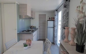 Eine moderne Küche mit Gasherd, Backofen und Kühlschrank. Es gibt einen Esstisch mit Stühlen, ein Fenster mit Vorhängen und dekorative Vasen auf der Fensterbank.