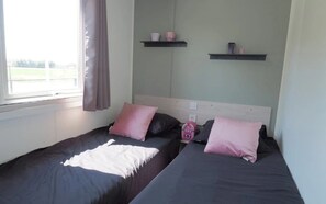 Ein Zimmer mit zwei Betten, einem fensterbelaubten Fenster und zwei Wandregalen mit Gegenständen.