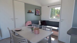 Un espace repas comprenant une table, des chaises, un canapé et une fenêtre donnant sur des arbres.