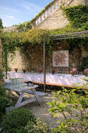 An outdoor dining area with a stone wall, wooden pergola, and a table set for a meal. - Cottage · Duplex with Pool (Saint Montan)