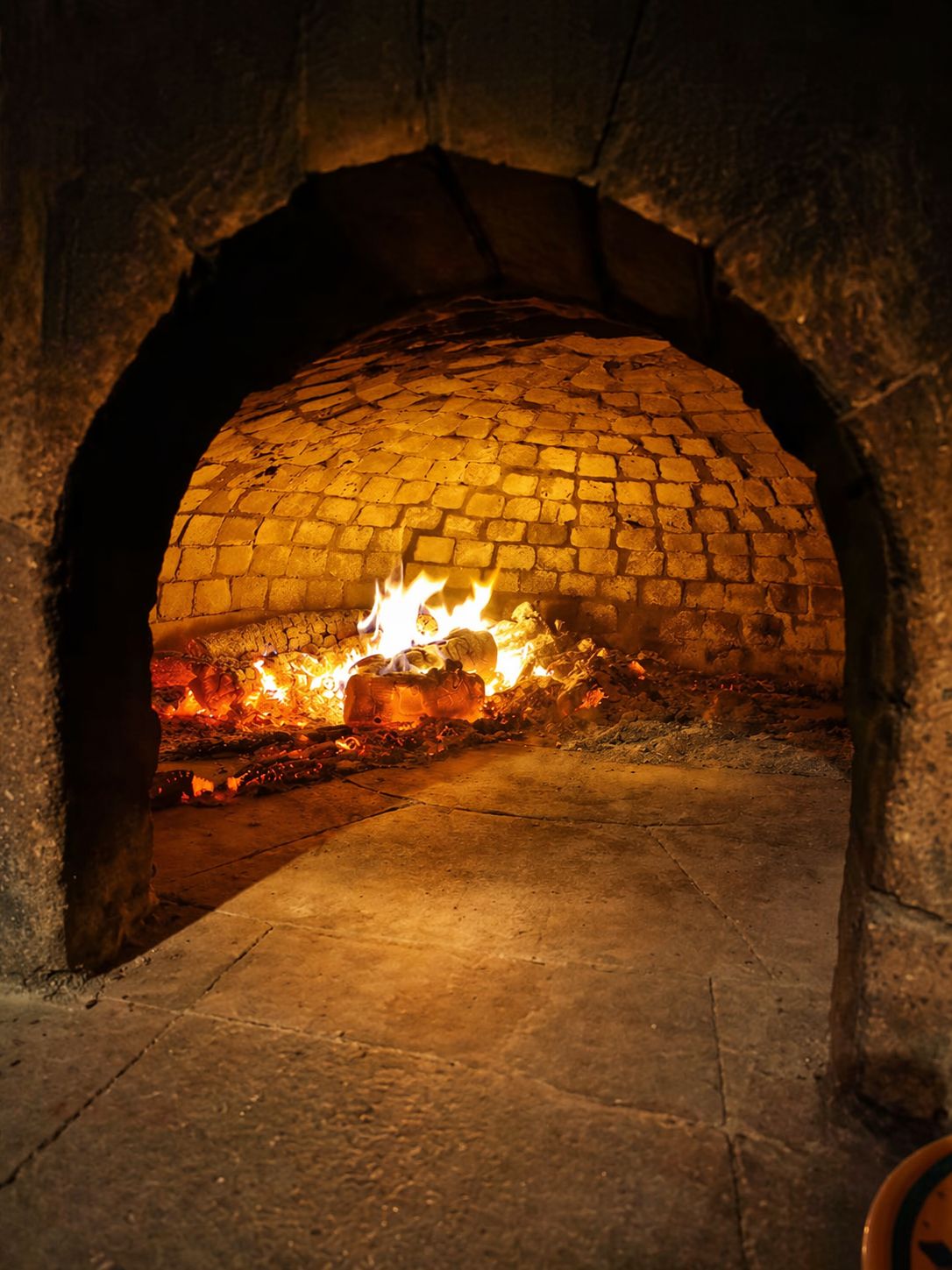 A stone oven with a fire burning inside, indicating a traditional cooking method.