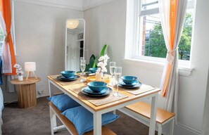 A dining area with a wooden table set for four, a mirror, and a window with curtains. - Boho Chic Studio Apartment, Next to CBD (Darlinghurst)
