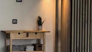 Canto com mesa consola de madeira, toalhas dobradas, planta em vaso e luminária fixada na parede.