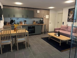 Un espacio habitable compacto con comedor, kitchenette y zona de estar con sofá y mesa de centro.