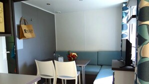 Ein gemütlicher Raum mit Küchenzeile, einem Essbereich mit zwei Stühlen, einem kleinen Tisch mit Obstschale und einer Couch.