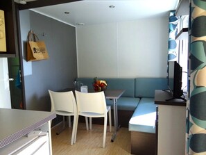 Ein gemütlicher Raum mit Küchenzeile, einem Essbereich mit zwei Stühlen, einem kleinen Tisch mit Obstschale und einer Couch.