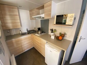 Eine kompakte Küche mit Holzausstattung, einer Mikrowelle, einem Spülbecken und einem kleinen Kühlschrank.