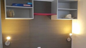 Ein Schlafzimmer mit einem Bett, einem Regal mit einer Monopoly-Schachtel, einer Lampe und einer Uhr.