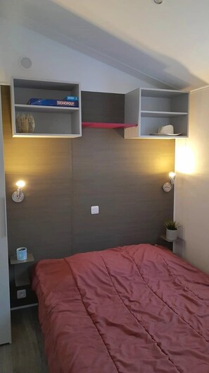 Ein Schlafzimmer mit einem Bett, einem Regal mit einer Monopoly-Schachtel, einer Lampe und einer Uhr.