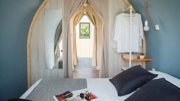 Een slaapkamer met een bed, kussens, een tijdschrift en een hanglamp.