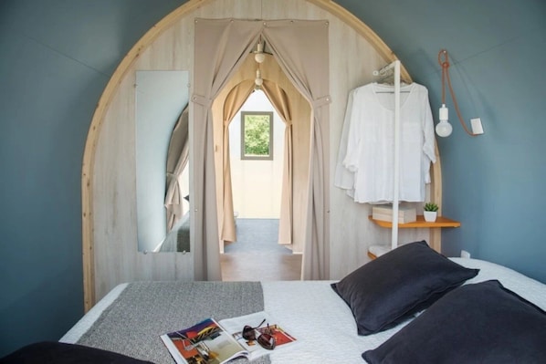 A bedroom with a bed, pillows, a magazine, and a hanging light fixture. - Camping 4 étoiles - Piscine  - ccbffab (Saint-Hilaire-de-Riez)