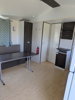 A compact room with a sofa, a small table, a kitchenette, and a fire extinguisher. - Camping 2 étoiles - ccbg00a (Sémeries)