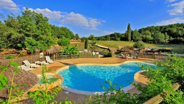 A swimming pool surrounded by lounge chairs and a wooden fence, with a view of a green landscape and trees. - Cabane 3 étoiles - Piscine  - ccbfgia (Saint-Amand-de-Coly)