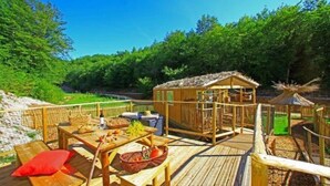 A wooden deck with picnic tables and a small wooden structure, surrounded by greenery. - Cabane 3 étoiles - Piscine  - ccbfgia (Saint-Amand-de-Coly)