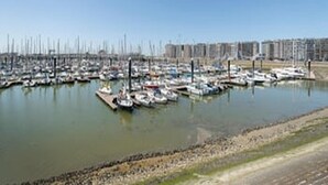 A marina with numerous boats docked, surrounded by a clear sky and a distant urban skyline. - Stunning Seaview Apartment With Balcony (Blankenberge)