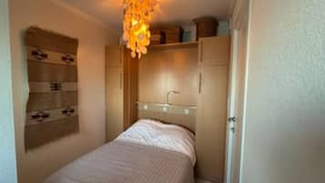 Un dormitorio con una cama, una mesita de noche, una lámpara colgante y armarios empotrados.
