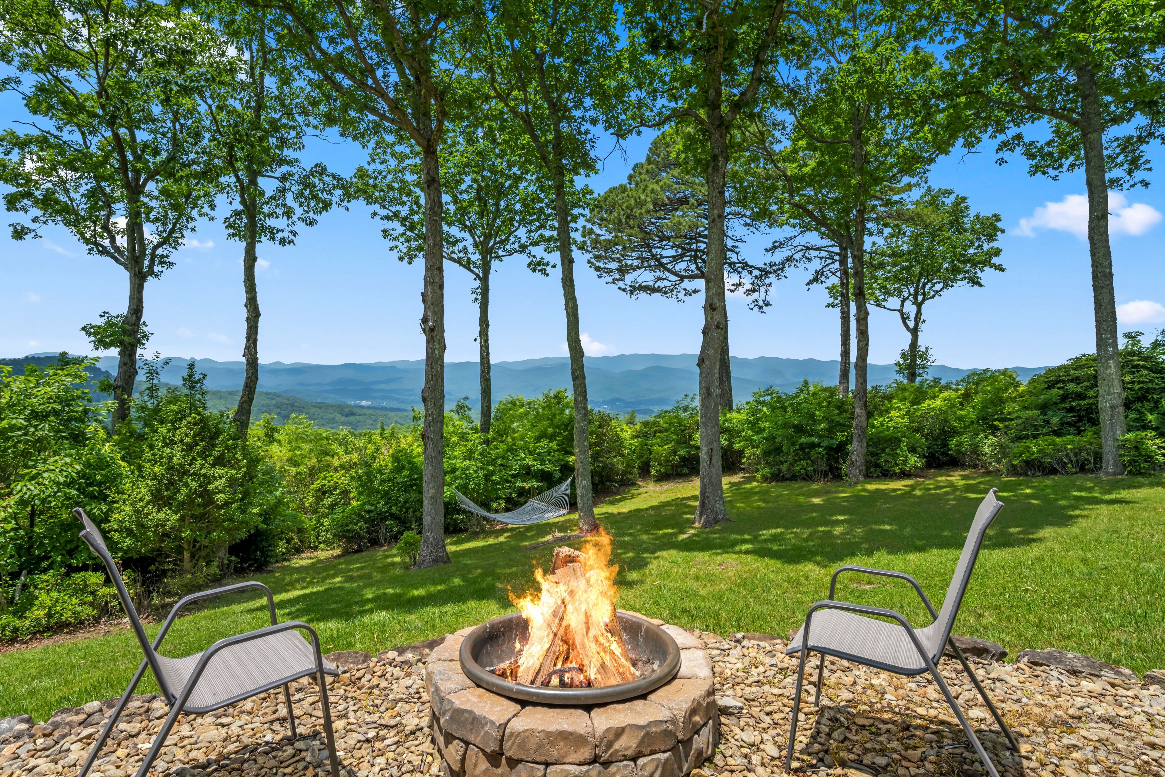 Un foyer extérieur avec deux chaises, entouré d’arbres et offrant une vue sur les montagnes.