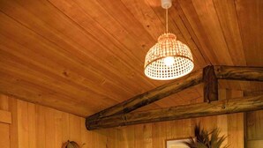 A wooden interior with a sofa, a chair, a table, a hanging light fixture, and a wall-mounted picture.