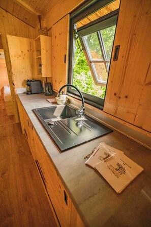 Une cuisine compacte dotée de meubles en bois, d’un évier en acier inoxydable et d’une fenêtre donnant sur un espace verdoyant.