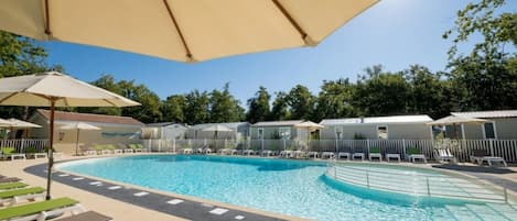 Piscina con sillas de descanso y sombrillas, rodeada de una valla y árboles.