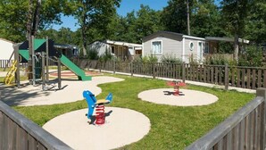 Un parc infantil amb cadenes i tobogan, envoltat d'una tanca de fusta i cases al fons.