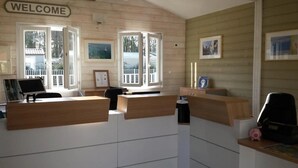 A reception desk with 'BIENVENUE' and 'WELCOME' signs, a window with a view of a house, and framed pictures on the wall. - Camping 4 étoiles - Piscine  - ccbffdb (Saint-Sulpice-de-Royan)