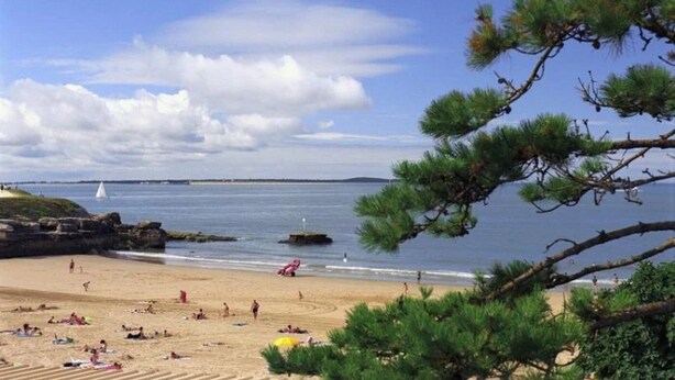A beach with people sunbathing and swimming, a sailboat in the distance, and rocky outcrops. - Camping 4 étoiles - Piscine  - ccbffdb (Saint-Sulpice-de-Royan)