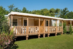 A row of wooden mobile homes with a covered porch and a grassy lawn. - Camping 4 étoiles - Piscine  - ccbffdb (Saint-Sulpice-de-Royan)