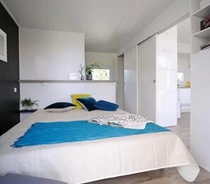 A bedroom with a bed, a window, a door, and a small table with a plant. - Camping 4 étoiles - Piscine  - ccbffdd (Saint-Sulpice-de-Royan)