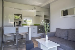 A modern kitchenette with a dining area, a grey sofa, and a white table with a vase. - Camping 4 étoiles - Piscine  - ccbffdd (Saint-Sulpice-de-Royan)