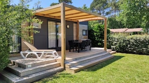 A modern outdoor patio with a wooden pergola, a dining table with chairs, and a small deck area. - Camping 4 étoiles - Piscine  - ccbffdd (Saint-Sulpice-de-Royan)